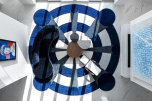 Aerial view of a modern minimalist living room in Florica with a blue target design, a rounded blue couch, nested accent tables, a lounge chair, and paintings on the wall.