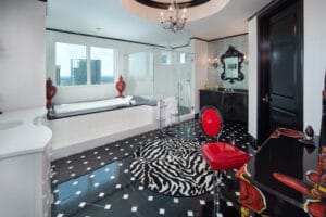 Modern eclectic design bathroom with mix of patterns and textures. Red and black laquer vanity with red leather chair, zebra print round rug on black and white square pattern tile floor, black sing and vanity with ornate black filigree mirror, white rectangular bathtub and white tile.