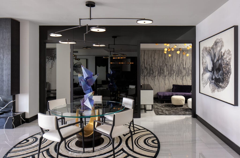 Custom luxury condo renovation in St. Pete. Dining area, den, living room. Geometric rug and sculpture, glass & brass dining table with metal and upholstered chairs, sculptural lighting, dark paint, organic painting.