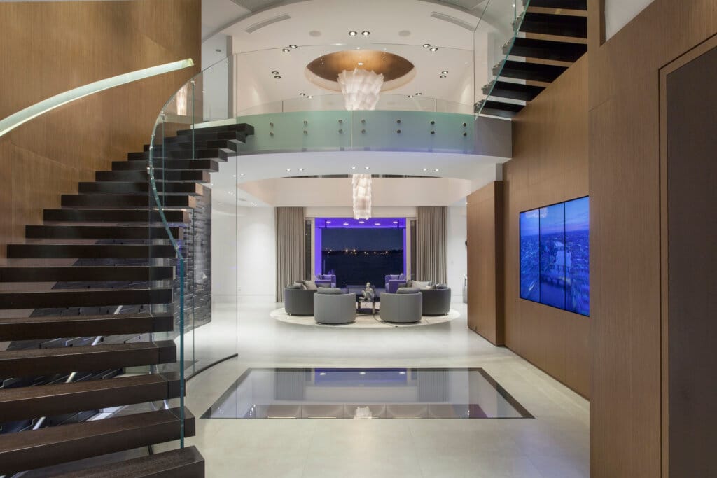 Dramatic entryway with an organic curved staircase, stone flooring, a clear window to the floor beneath, metal and glass double doors