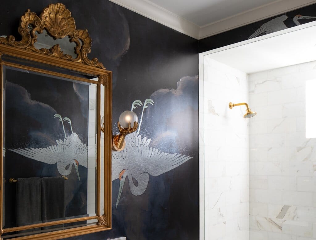 Luxury bathroom featuring a gilded mirror layered over marble surfaces and specialty wallpaper featuring a crane by Rob Bowen Design Group.