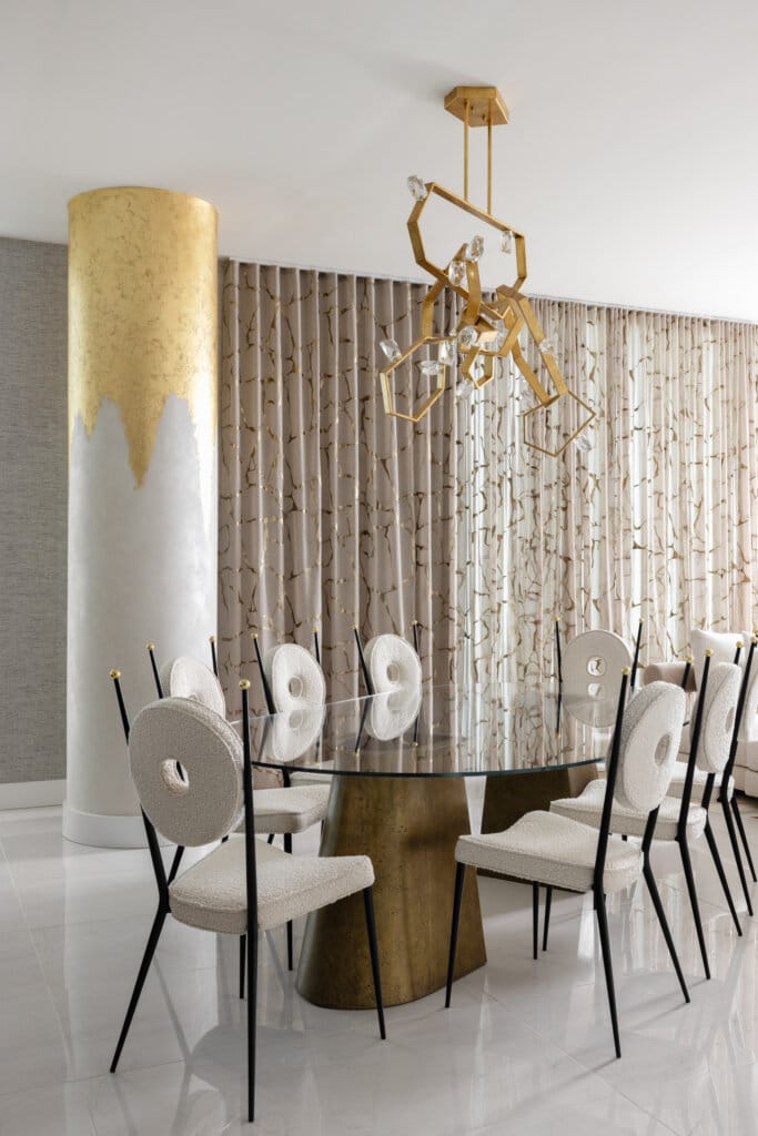 Tampa Bay luxury dining room with glass top table, modern upholstered dining chairs with circular backs, column with gold leaf, gold geometric chandelier