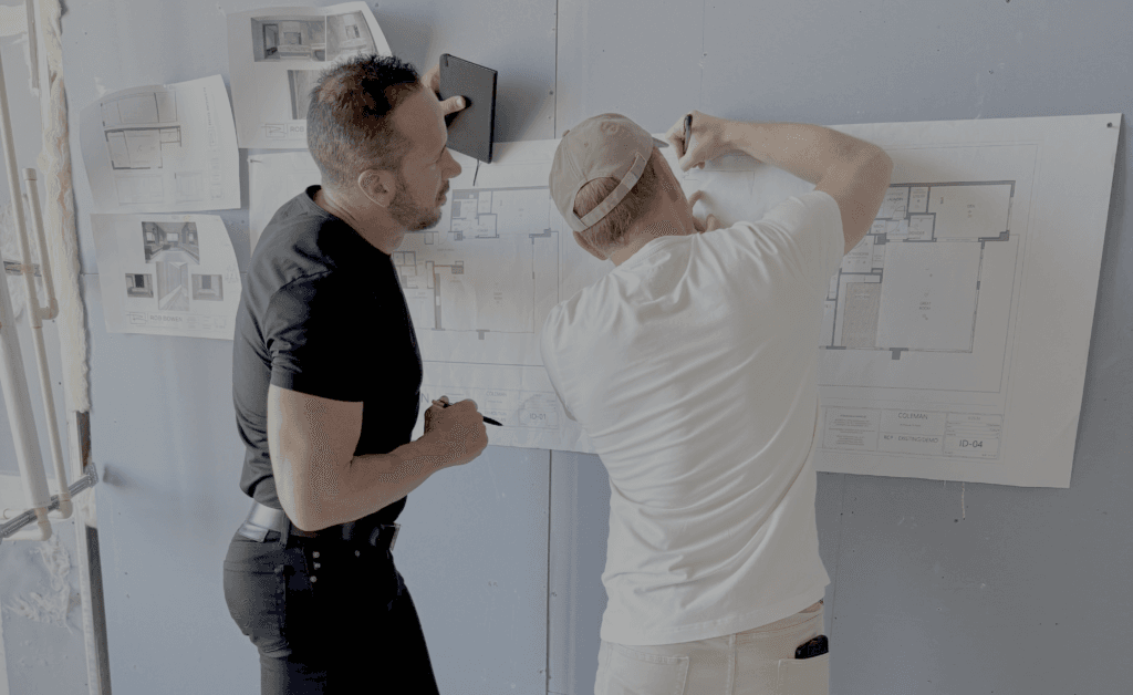 Two people, including Tampa luxury interior designer Rob Bowen, examine blueprints and architectural drawings pinned to a wall.