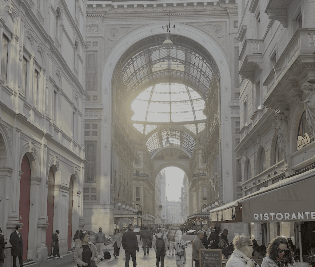 The Galleria Vittorio Emanuele II in Milan, Italy. A sunlit view down a grand arcade with people walking and shops lining the sides.